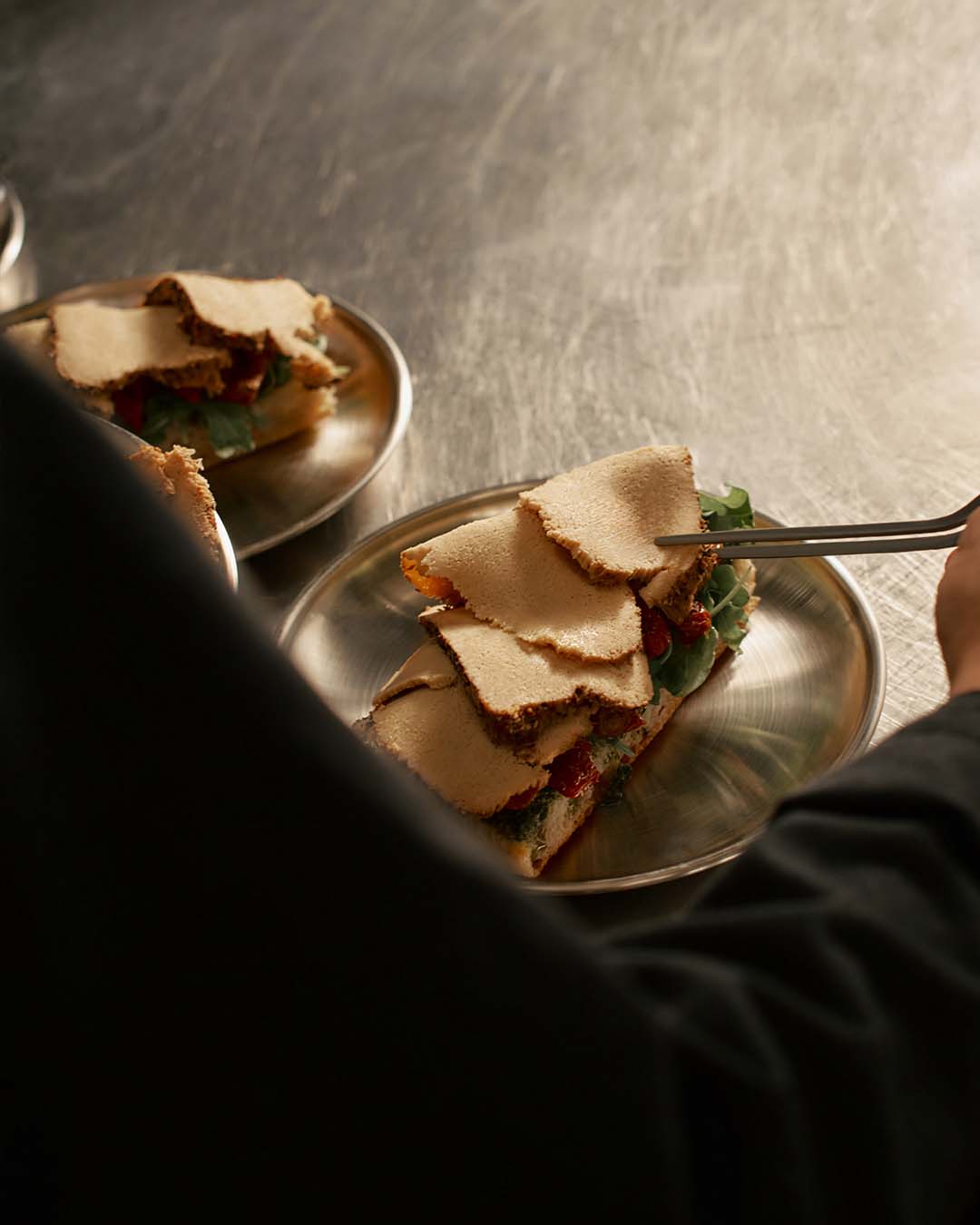A chef cooking a focaccia toast with arugula, tomatoes and Novameat cold cut turkey style in professional kitchen for food service